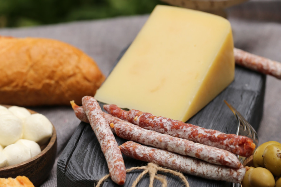 Verschiedene Delikatessen auf einem Tisch: Ein großes Stück Käse, mehrere Mini-Salami-Sticks
